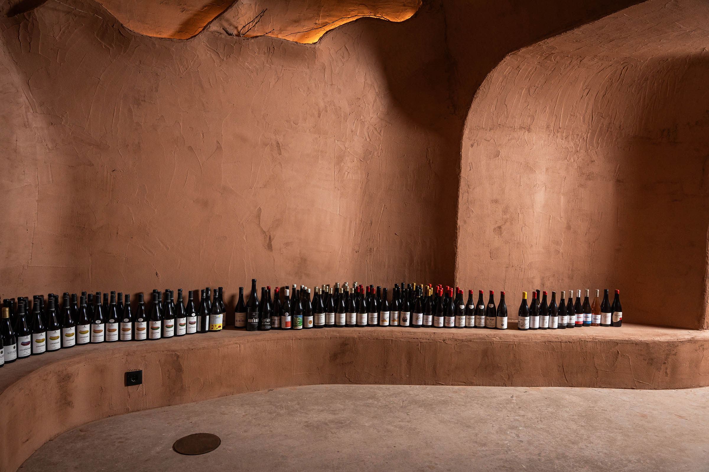 La bodega de BARRO: cuevas de adobe con botellas alineadas sobre una repisa curva