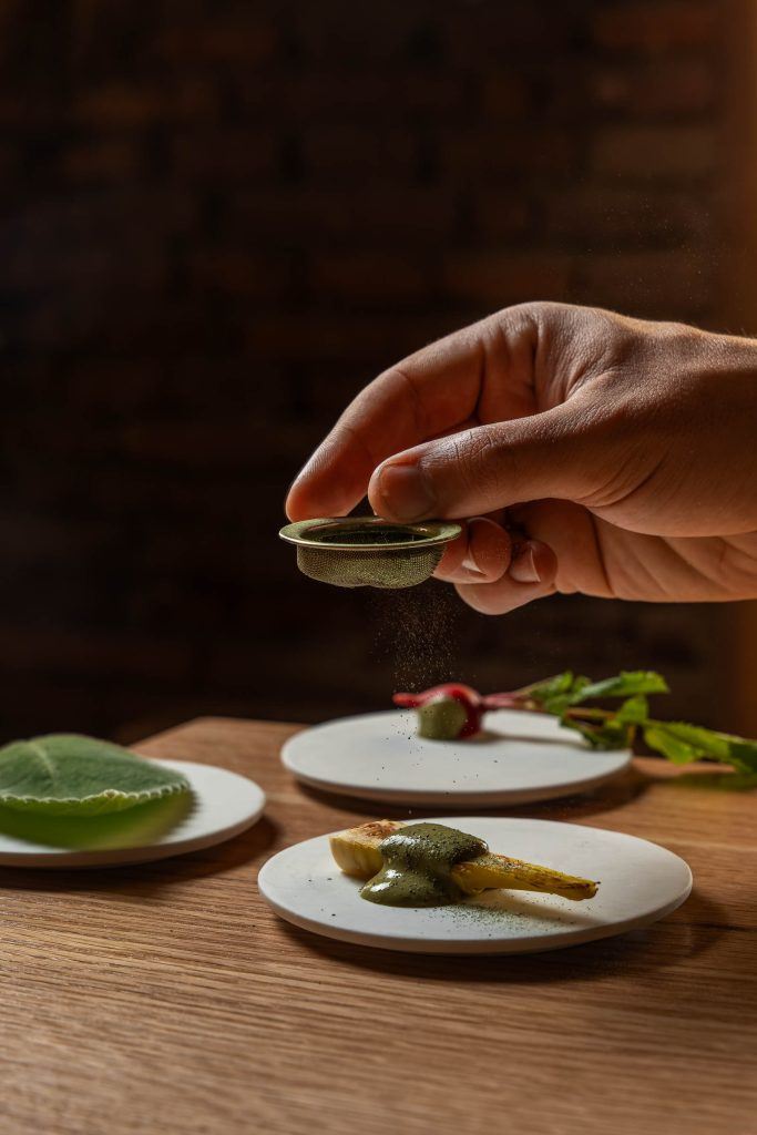Una mano espolvorea sobre platos de cerámica blanca, con el ladrillo de la harinera al fondo